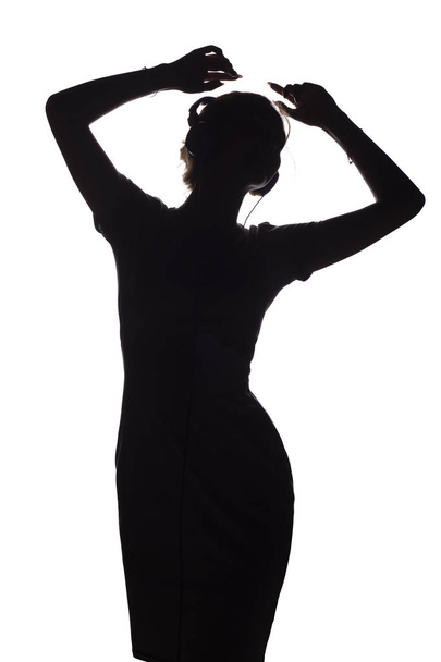 silueta de una chica activa escuchando música en auriculares, figura de una joven bailando con las manos en alto sobre un fondo blanco aislado
 - Foto, imagen