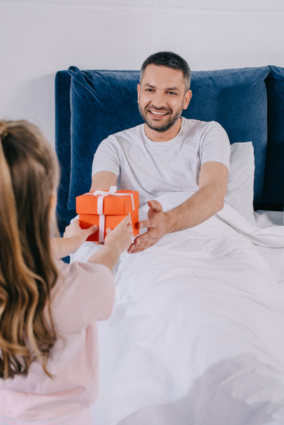 daughter presenting father day gift box to happy dad sitting under blanket - Fotoğraf, Görsel