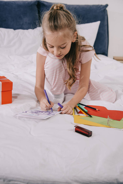 cute child drawing on fathers day greeting card while sitting on bedding - Фото, зображення