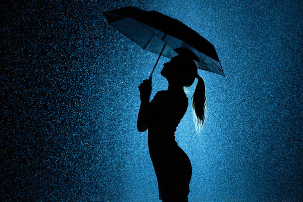 silhouette of the figure of a young girl with an umbrella in the rain - Фото, зображення