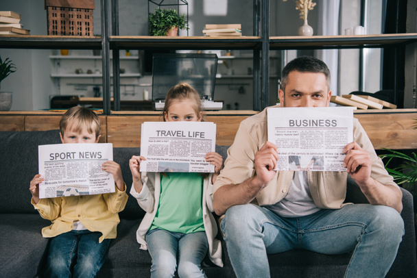 χαρούμενο πατέρα και παιδιά που κρατούν εφημερίδες ενώ κάθονται στον καναπέ στο σπίτι - Φωτογραφία, εικόνα