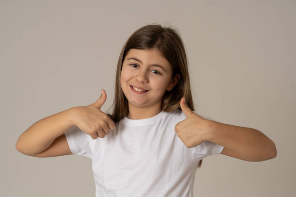 Portrait of young schoolgirl feeling happy smiling and making thumbs up gesture. Isolated on neutral background. In Education Children, Human expressions and body language. - Foto, afbeelding