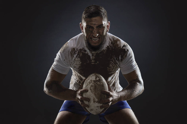 Karanlık arka planda rugby topu ile izole kirli rugby oyuncusu - Fotoğraf, Görsel