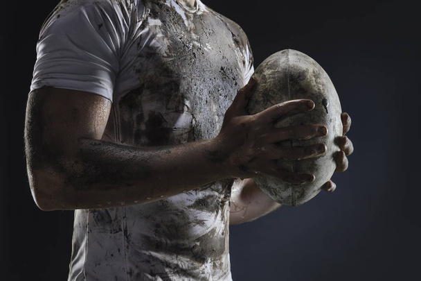 Rugby speler handen met bal op donkere achtergrond. Close-up - Foto, afbeelding