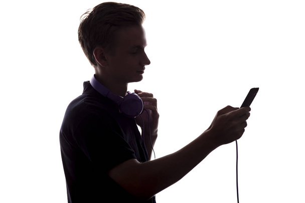 silhueta de um jovem com fones de ouvido em seu pescoço, um cara vira através de uma lista de reprodução de música em seu jogador em fundo isolado branco
 - Foto, Imagem
