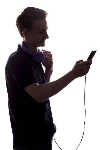 silueta mladého mužového profilu se sluchátky na krku a MP3 přehrávač v ruce, teenagerky se propijí seznamem hudby na bílém izolovaném pozadí, koncept životního stylu mládeže - Fotografie, Obrázek