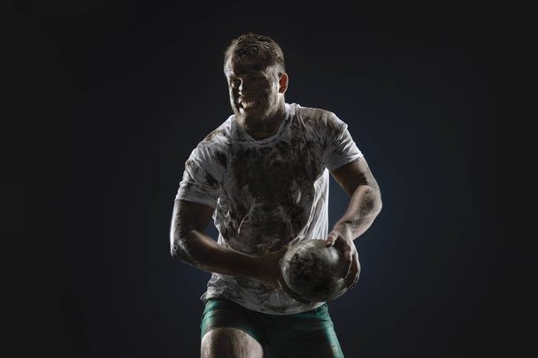 Geïsoleerde vuile rugbyspeler met Rugby bal op donkere achtergrond - Foto, afbeelding