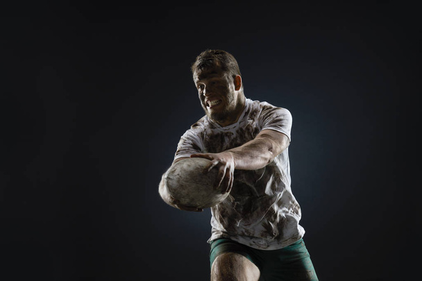 Odizolowany brudny zawodnik rugby z piłką rugby na ciemnym tle - Zdjęcie, obraz