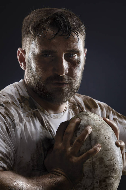 Isolated dirty rugby player with rugby ball on dark background - Foto, Bild