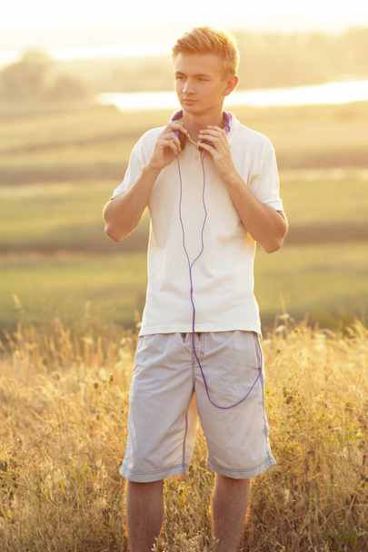 teenager in headphones listening to music on nature, young man resting in summer field, concept sport and music - Fotografie, Obrázek