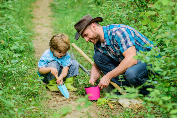 Gardening hobby. Dad teaching little son care plants. Spring gardening routine. Planting flowers. Little helper in garden. Farm family. Little boy and father in nature background. Gardening tools - Фото, зображення