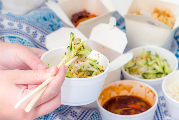 Syöminen kiinalainen ottaa pois ruokaa pilkkoa tikkuja kotona lakanat taustalla. Mausteinen aasialainen ruoka valkoisessa laatikossa salaatti, souse, riisi muna, kuiva naudanliha, rapea kana, joka on keitetty öljyssä
 - Valokuva, kuva