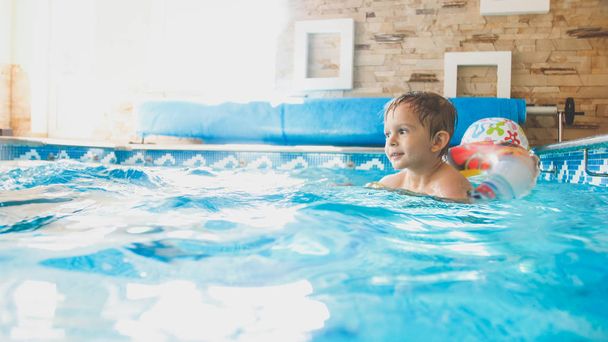 Portrait d'heureux garçon joyeux tout-petit jouant avec ballon de plage gonflable et anneau coloré à la piscine intérieure dans la maison
 - Photo, image