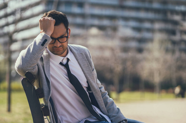 Young businessman is sitting in park after being fired. He is depressed. - 写真・画像