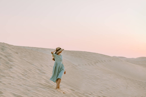 Mladá žena kráčí po písečných dunách v poušti během západu slunce - Fotografie, Obrázek
