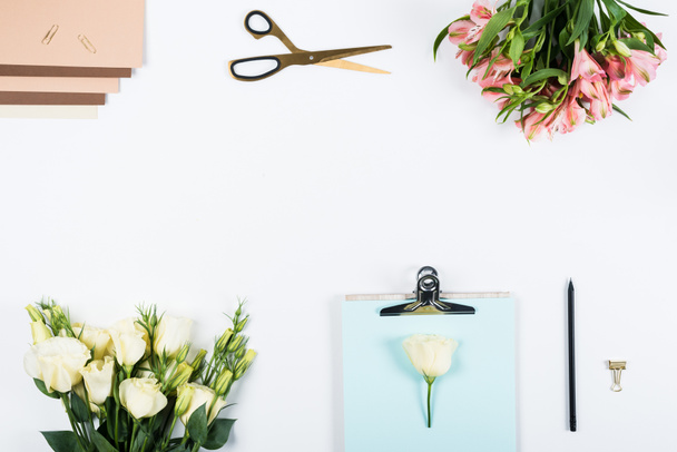 επάνω όψη του Προχείρου, λουλούδια, ψαλίδι, πένα, συνδετήρες χαρτιού, κλιπ ντοσιέ και χαρτί χειροτεχνίας σε λευκό - Φωτογραφία, εικόνα