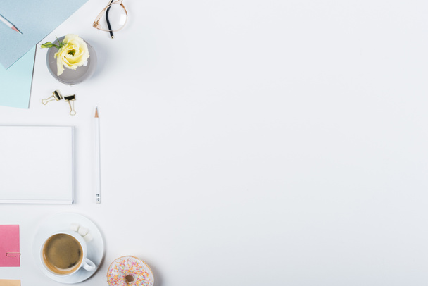 Κορυφαία θέα του φλιτζάνι του καφέ, ντόνατ, βιβλίο, μολύβια, γυαλιά και κλιπ ντοσιέ σε λευκό - Φωτογραφία, εικόνα