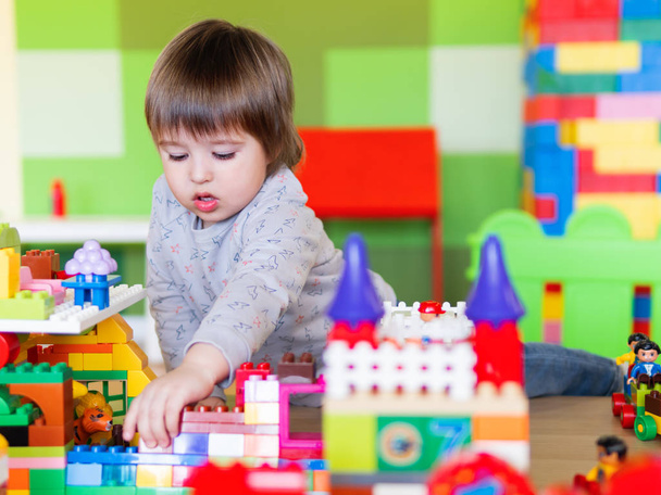 Peuter jongen speelt in kinderkamer met kleurrijke constructeur. Educatief speelgoed blok in zijn handen. Kind is bezig met speelgoed bakstenen. - Foto, afbeelding