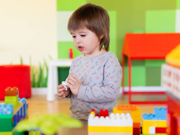 Toddler boy is playing in kidsroom with colorful constructor. Educational toy block in his hands. Kid is busy with toy bricks. - Valokuva, kuva