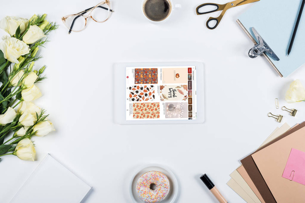 KYIV, UKRAINE - MAY 11, 2019: top view of cup of coffee, doughnut, flowers, glasses, book, papers, clipboard and digital tablet with pinterest app on screen on white - Fotoğraf, Görsel