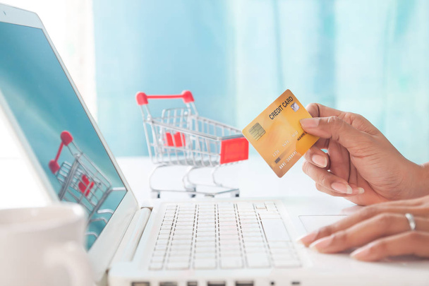 Eller kredi kartı tutarak ve alışveriş sepeti arka plan ile dizüstü bilgisayar kullanarak. Online alışveriş, E-ödeme veya internet bankacılığı - Fotoğraf, Görsel