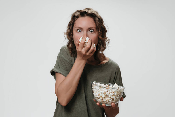 Молодая женщина с вьющимися волосами ест попкорн, смотрит фильм ужасов
 - Фото, изображение