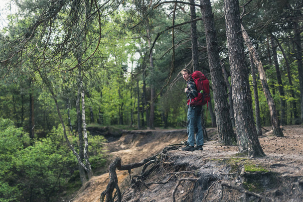 Young man with red backpack at edge of canyon in spring forest. - Foto, afbeelding