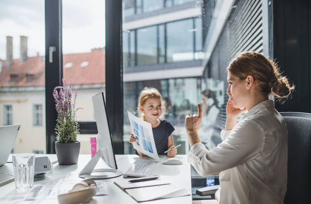 A businesswoman with small daughter sitting in an office, working. - Foto, Bild