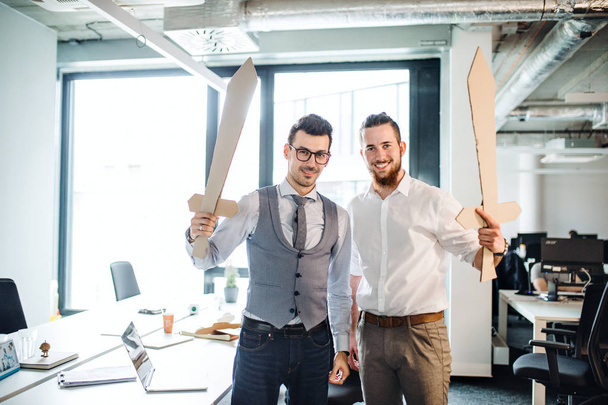 Two young businessmen with swords in an office. A competition concept. - Photo, Image