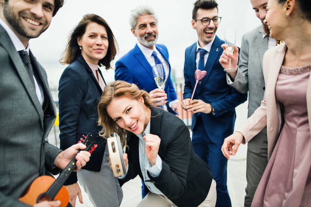 A group of joyful businesspeople having a party outdoors on roof terrace in city. - 写真・画像