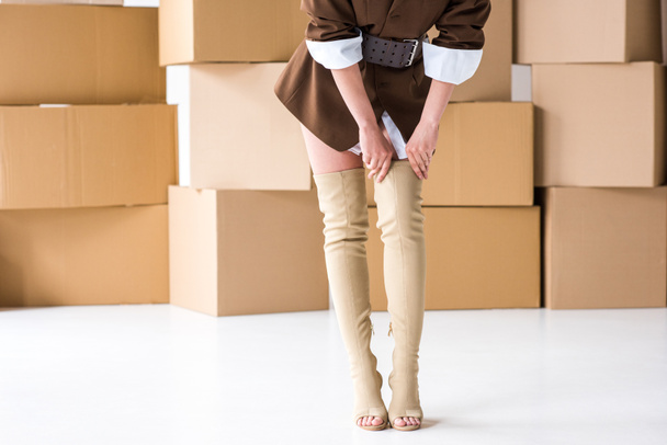 cropped view of girl touching boots while standing near boxes on white  - Photo, Image