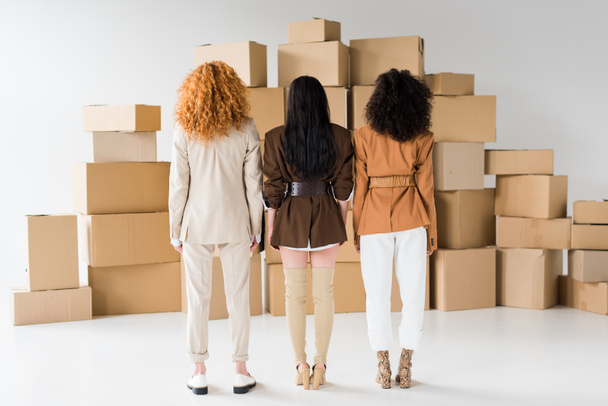back view of redhead girl standing with stylish african american women near boxes on white  - Foto, imagen