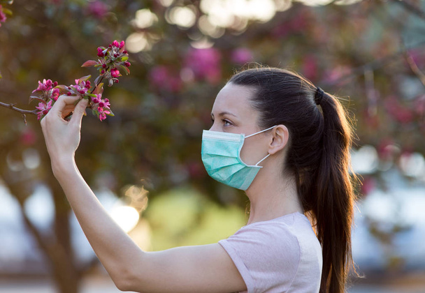 Woman with mask beside blooming tree - Photo, Image