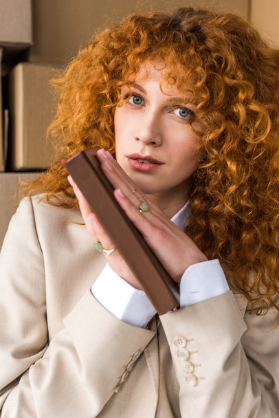 attractive redhead girl holding book near cardboard boxes  - Фото, зображення