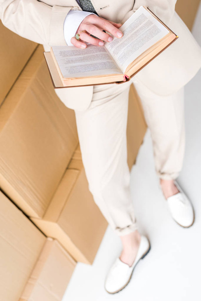 bovenaanzicht van de vrouw in formele slijtage staande met boek in de buurt van dozen op wit  - Foto, afbeelding