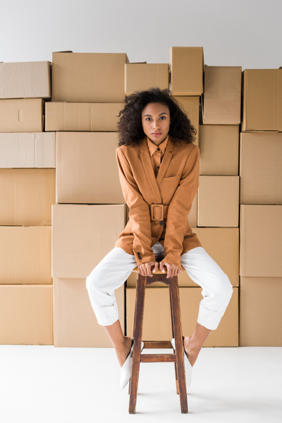 attractive african american girl sitting on wooden chair and looking at camera on white  - Photo, image