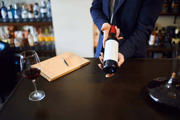 άνθρωπος σε φόρμα προσφέρει τέλειο κρασί για τους πελάτες, τους πελάτες - Φωτογραφία, εικόνα