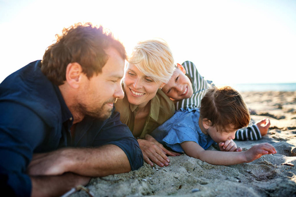 Young family with two small children lying down outdoors on beach. - Photo, image
