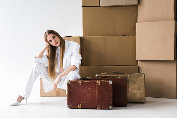 attraktive blonde Frau posiert in der Nähe von Koffern und Kartons auf weiß  - Foto, Bild