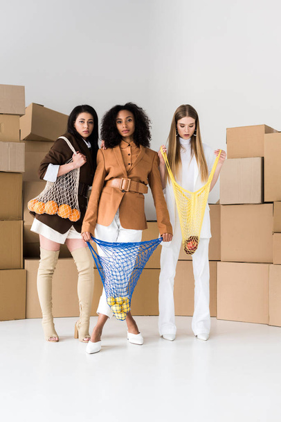 Африканские американские девушки держат струнные сумки с фруктами рядом блондинка женщина и коробки на белом
  - Фото, изображение