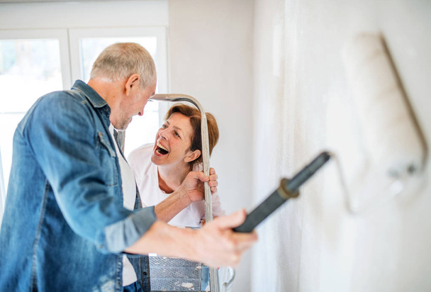 Senior couple painting walls in new home, relocation concept. - Φωτογραφία, εικόνα