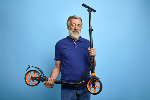 good looking mature man holding scooter and looking at the camera - Zdjęcie, obraz