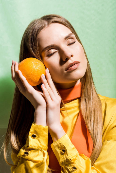 vonzó szőke nő csukott szemmel tartó narancssárga, zöld  - Fotó, kép