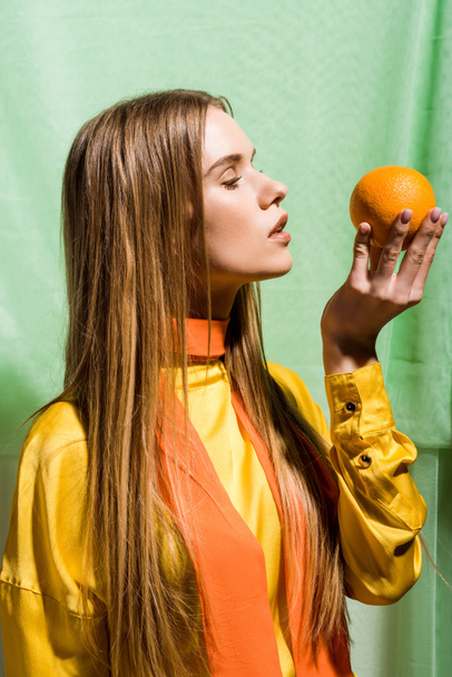 beautiful blonde young woman looking at orange on green  - Φωτογραφία, εικόνα