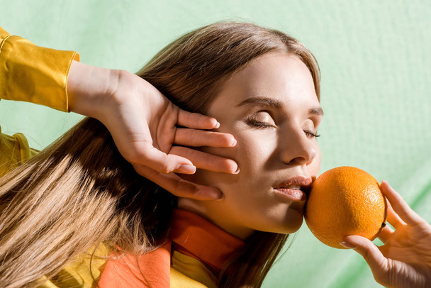 piękny blond kobieta z zamkniętymi oczami trzymając pomarańczowy na zielono  - Zdjęcie, obraz