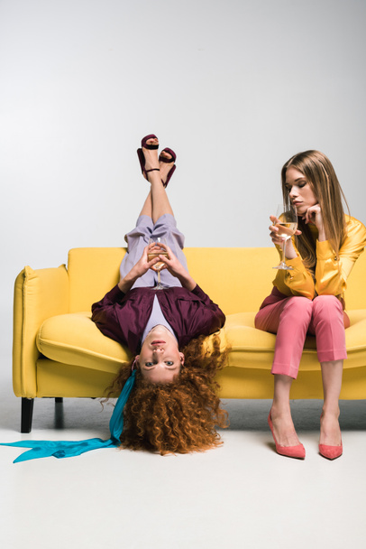 рыжая девушка лежит на диване рядом с блондинкой с бокалом шампанского на белом
  - Фото, изображение