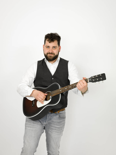 mies, jolla on musta tukka ja parta pelaa akustista kitaraa valkoisella taustalla
 - Valokuva, kuva