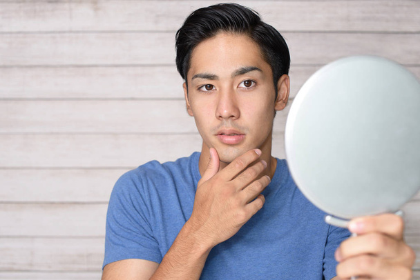 aziatische man kijken naar zijn gezicht in spiegel - Foto, afbeelding