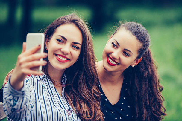 Dwie piękne młode kobiety robią selfie na zewnątrz - Zdjęcie, obraz