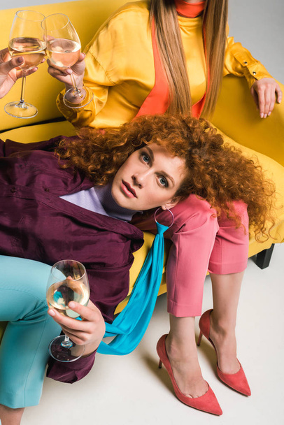 vista aerea di attraente donna rossa sdraiata sul divano e in possesso di bicchiere di champagne vicino alle ragazze sul bianco
  - Foto, immagini